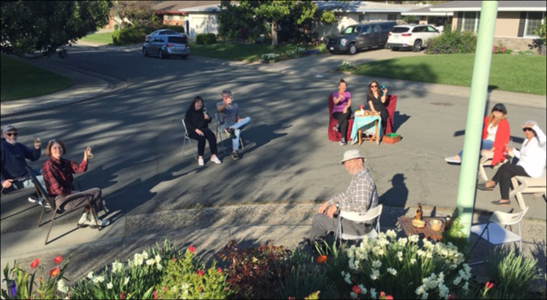 A photo of a group of neighbors getting together  in the street with all their chairs carefully placed 6' apart.